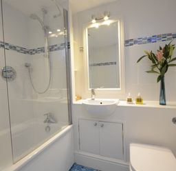 A bathroom with a bathtub shower combination a sink a mirror and a vase with flowers at Pied a Mer Aldeburgh in Aldeburgh