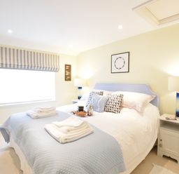 A bedroom with a double bed blue bedspread pillows bedside tables lamps and a window with striped blinds at Pied a Mer Aldeburgh