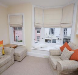 A sitting room with two plaid sofas orange and yellow cushions a bay window with cushions and beige blinds a floor lamp and wooden side tables at The Hideaway Aldeburgh
