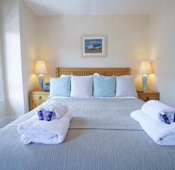 A bedroom with a double bed with blue and white pillows bedside tables with lamps and folded towels at The Hideaway in Aldeburgh