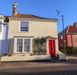 A two-story cream brick house with a red front door and windows near the street at Winkle Cottage Aldeburgh