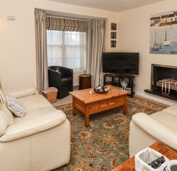 A living room with cream leather sofas a wooden coffee table a television near a fireplace and striped curtains at Winkle Cottage in Aldeburgh