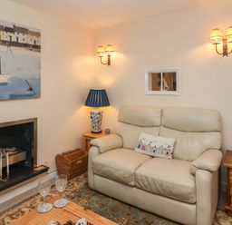 A living room with a cream leather sofa a wooden coffee table a fireplace and a painting above at Winkle Cottage Aldeburgh