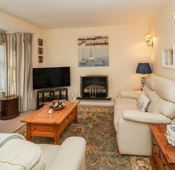 A living room with cream sofas coffee table television and fireplace at Winkle Cottage Aldeburgh