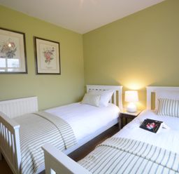 A bedroom with two single beds white bedding striped blankets and pillows bedside table with lamp and framed floral prints on the wall at Rookyards Spexhall Near Halesworth