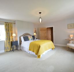 A bedroom with a bed with yellow blanket curtains by the window bedside tables with lamps an armchair and wooden door at Rookyards in Spexhall Near Halesworth