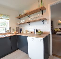 A kitchen with wooden countertops open shelves with dishes and glassware and a white dishwasher at Rookyards Spexhall Near Halesworth