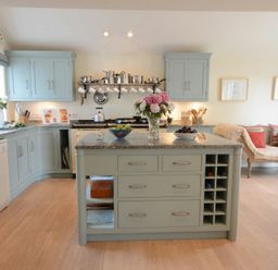 A kitchen with blue cabinets an island with flowers and bowls and a seating area with a bench at 2 The Bays Thorpeness