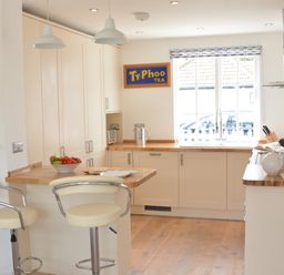 A kitchen with bar stools a fruit bowl and a Ty-Phoo tea sign on the wall at 4 The Dunes Thorpeness