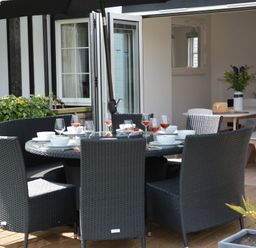 An outdoor dining area with a round table set with bowls and glasses and black wicker chairs at 4 The Dunes Thorpeness