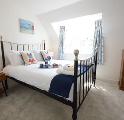 A bedroom with a metal bed frame bedside table with lamp wooden chest of drawers and window with curtains at 4 The Dunes Thorpeness