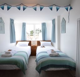 A bedroom with two single beds with folded towels on them and a window with blue curtains at 4 The Dunes Thorpeness