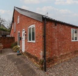 An exterior view of a brick building with a white door and windows and an outdoor wooden table set on gravel at 1 The Old Coach House Huntingfield Near Laxfield