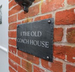 A brick wall with a black plaque reading 1 The Old Coach House next to a white door at 1 The Old Coach House Huntingfield Near Laxfield