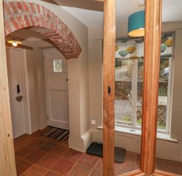 An entryway with a brick archway a white door a striped rug tile flooring and a window with a teal lamp at 1 The Old Coach House Huntingfield Near Laxfield