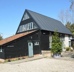 A black barn style house with light blue doors and windows surrounded by trees and plants at Yew Tree Farm Barn Worlingworth near Framlingham