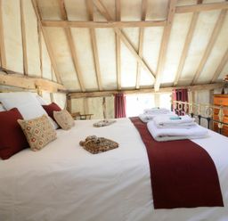 A bedroom with a bed made with white sheets and red runners near a wooden dresser and a window at Yew Tree Farm Barn Worlingworth