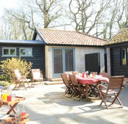 An outdoor patio area with wooden chairs and tables with a red tablecloth and drinks at Yew Tree Farm Barn Worlingworth