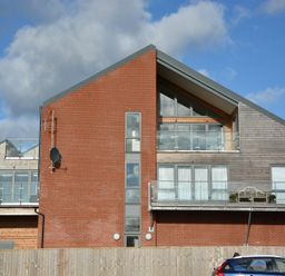 A modern building with brick and wood exterior and glass balconies with a blue car in front at King George Penthouse in Aldeburgh