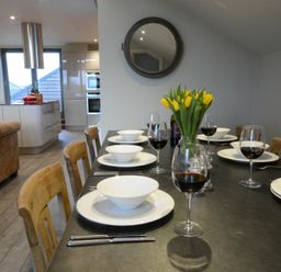 A dining table set with white bowls plates wine glasses and yellow flowers in a kitchen area at King George Penthouse in Aldeburgh