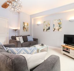 A living room with two gray sofas a coffee table a television on a wooden stand and abstract paintings on the walls at Saffron Blythview in Blythburgh near Southwold