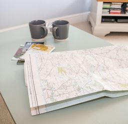 A table with two mugs a folded map and some booklets in a room with a white cabinet holding DVDs at Saffron Blythview in Blythburgh near Southwold