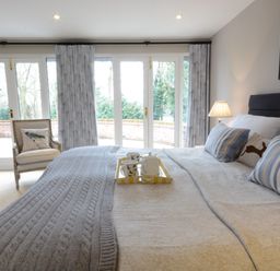 A bedroom with a large bed, striped pillows, a chair with a bird cushion, and glass doors leading outside at Bird Cottage, Burgh Near Grundisburgh