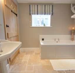A bathroom with a bathtub a sink a wooden door and a window with striped blinds at Bird Cottage Burgh Near Grundisburgh
