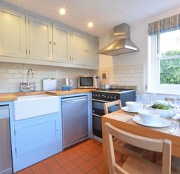 A kitchen with wooden countertop white cabinets dining table set with bowls glasses and a bottle at 1 South Cottages in Thorpeness
