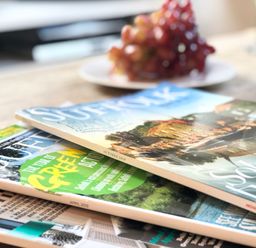 A wooden table with a stack of magazines and a plate of grapes in the background at 1 South Cottages in Thorpeness