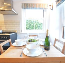 A dining table set with bowls plates glasses and a bottle of champagne in a kitchen at 1 South Cottages in Thorpeness