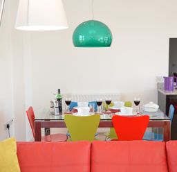 A dining area with a glass table set for four with colorful chairs and a green pendant light above at Parrotfish Bay Southwold