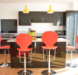 A kitchen with four red bar stools and black cabinets at Parrotfish Bay in Southwold