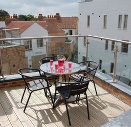 A balcony with a round metal table and four black chairs with glasses and a pitcher of red drink at Seal Cove in Southwold