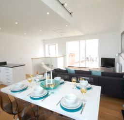 A dining table set for six with plates and glasses in a modern open-plan kitchen and living area at Seal Cove in Southwold