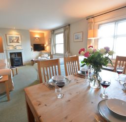 A dining table set with plates glassware and flowers in a living room with sofas a fireplace and a television at Crabbe House in Aldeburgh