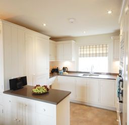 A kitchen with white cabinets a gray countertop a plate of grapes a window with a checkered blind and kitchen appliances at Crabbe House in Aldeburgh