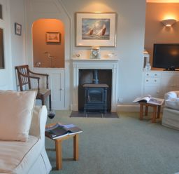A living room with armchairs a fireplace a television and small wooden tables at Crabbe House in Aldeburgh