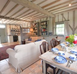 An open living space with a wooden dining table set with blue and white dishes a sofa bookshelves and a kitchen area at The Gig House Stowupland