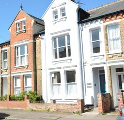 A row of attached houses with brick and white facades and parked cars on the street at Spindrift Southwold
