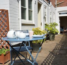 A patio with a blue metal table and chair set with teapots and cups beside a white brick wall with potted plants at Spindrift Southwold