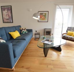 A living room with blue sofa and patterned armchair facing a glass coffee table at Aldeburgh Lodge Gardens in Aldeburgh