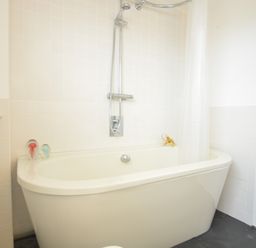 A bathroom with a bathtub shower and white tiled walls with two glass decorations at Aldeburgh Lodge Gardens in Aldeburgh