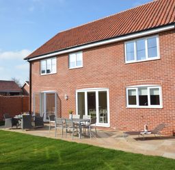 A backyard patio with tables chairs and a lounge chair outside a brick house with tiled roof at Meadowsweet Blythburgh near Reydon