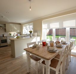 A kitchen and dining area with a wooden table set for breakfast and a view of the garden through glass doors at Meadowsweet Blythburgh in Blythburgh near Reydon