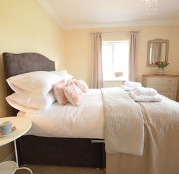 A bedroom with a made bed pillows and towels bedside table with a lamp and cup chest of drawers with a mirror and flowers Meadowsweet Blythburgh Blythburgh near Reydon