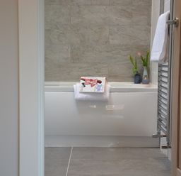 A bathroom with a white bathtub a towel hanging on the side and flowers in vases on the edge at Milk Parlour Spexhall Near Halesworth
