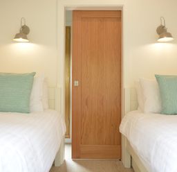 A bedroom with two single beds with white bedding and green pillows and a wooden sliding door in between at Red Poll Barn Spexhall Near Halesworth