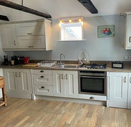 A kitchen with white cabinets a stainless steel oven a gas stove a sink a toaster kettle coffee maker and a wooden table at Walton House Southwold