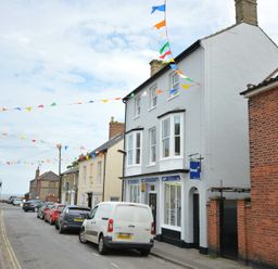 A street with parked cars and buildings with colorful flags hanging above at Walton House Southwold
